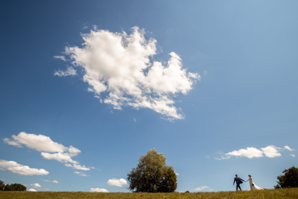 Les mariés marchent sur une crête sous un ciel bleu et ses nuages